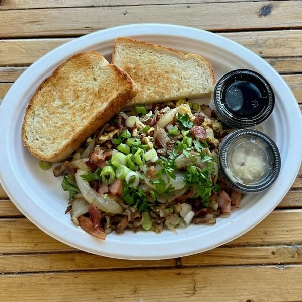 A breakfast plate with scrambled eggs, bacon, onions, green onions, parsley, toast, and two dipping sauces.